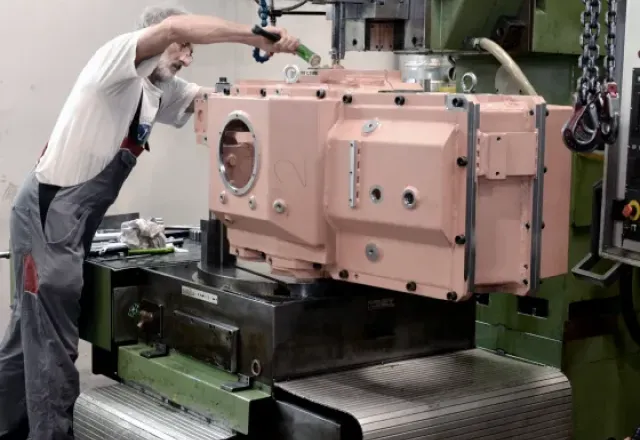 Arbeiter bedient eine große rosa Metallpresse in einer Werkhalle.
