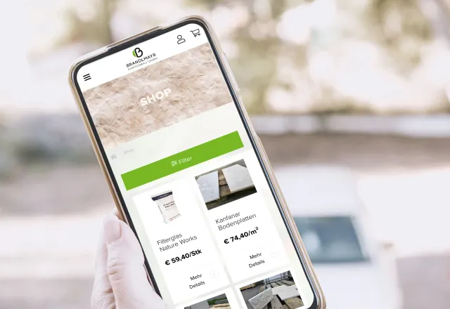 Smartphone mit geöffneter Immobilien-App wird vor einer Straße mit Häusern gehalten.