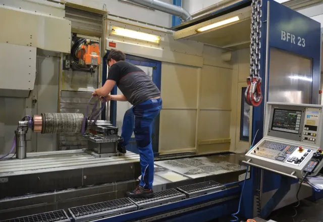 Mitarbeiter bearbeitet ein Metallteil an einer großen CNC-Drehmaschine.