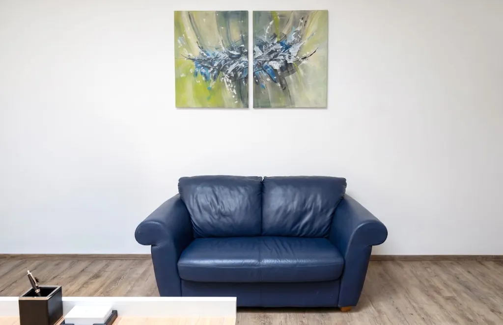 Wohnzimmer mit blauem Ledersofa, Holzboden und abstraktem Wandbild.